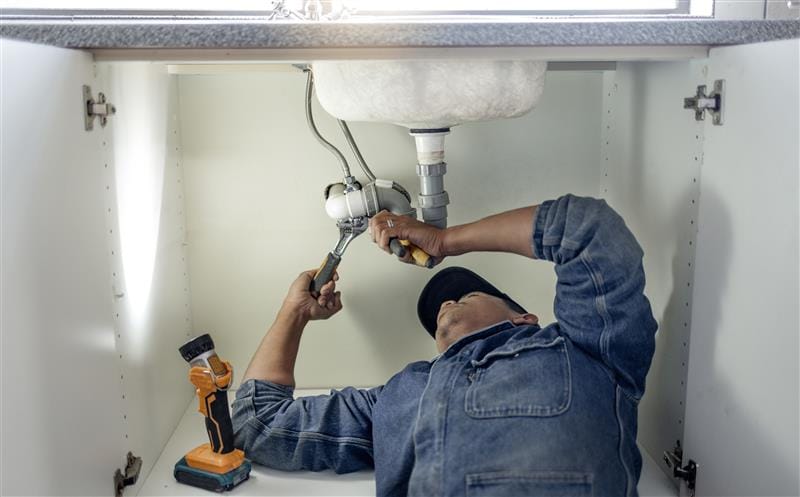 Plumber repairing pipes beneath a bathroom sink in Hayward